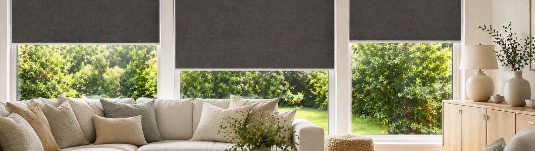 Yaringa textured blackout roller blinds in charcoal grey installed in a modern New Zealand living room, featuring large windows, soft natural light, and contemporary neutral interior styling.